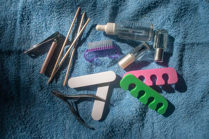 Side view of hands holding precision nail art tools with polished nails, against a clean white studio backdrop